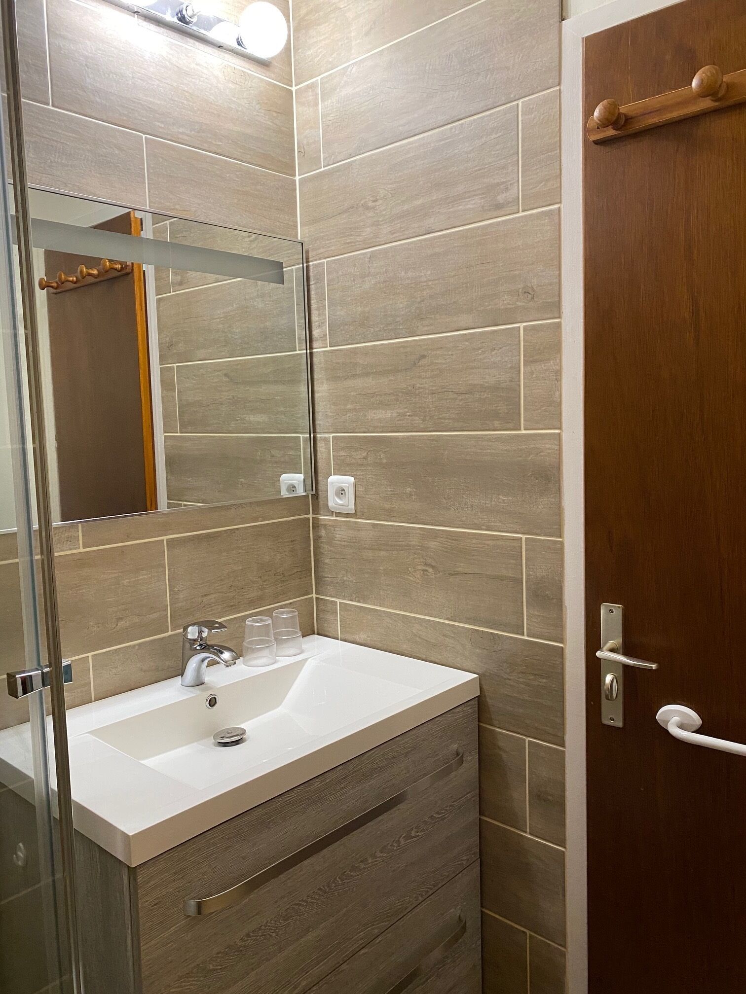 A bathroom with a white sink, a mirror, and wooden tiles.