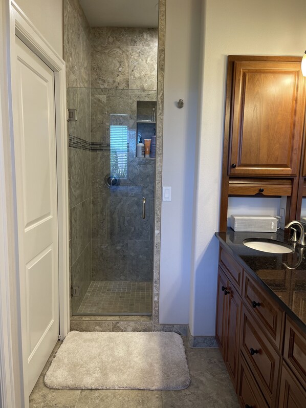 A bathroom with a glass shower enclosure, a wooden vanity with a sink, and a white rug on the floor. - Elevated R & R in Desert Aire! (Desert Aire)