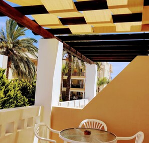 Un espacio al aire libre cubierto con una mesa, sillas, palmeras y un edificio al fondo.