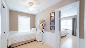 A bedroom with a bed, a ceiling fan, a bedside table with a lamp, and a wall with framed pictures. - Beautiful Lavallette Home - Perfect for Family and Friends (Lavallette)