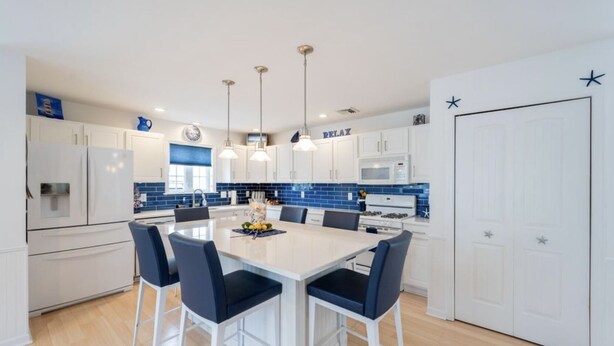 A modern kitchen with white cabinets, a central island with chairs, and pendant lighting. - Beautiful Lavallette Home - Perfect for Family and Friends (Lavallette)
