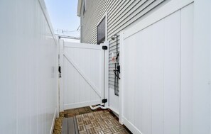 A narrow outdoor space with a white fence, a small wooden deck, and a metal gate. - Beautiful Lavallette Home - Perfect for Family and Friends (Lavallette)
