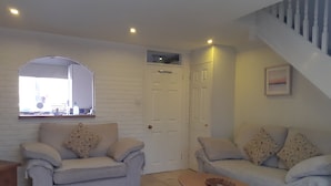 Ein Wohnzimmer mit zwei Sofas, einem Couchtisch, einem gemusterten Teppich, einer weißen Tür und einer Treppe.