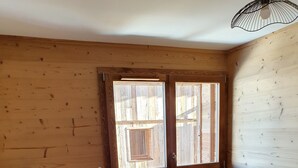 Una habitación de cabaña de madera con una cama, un pequeño banco y una ventana.