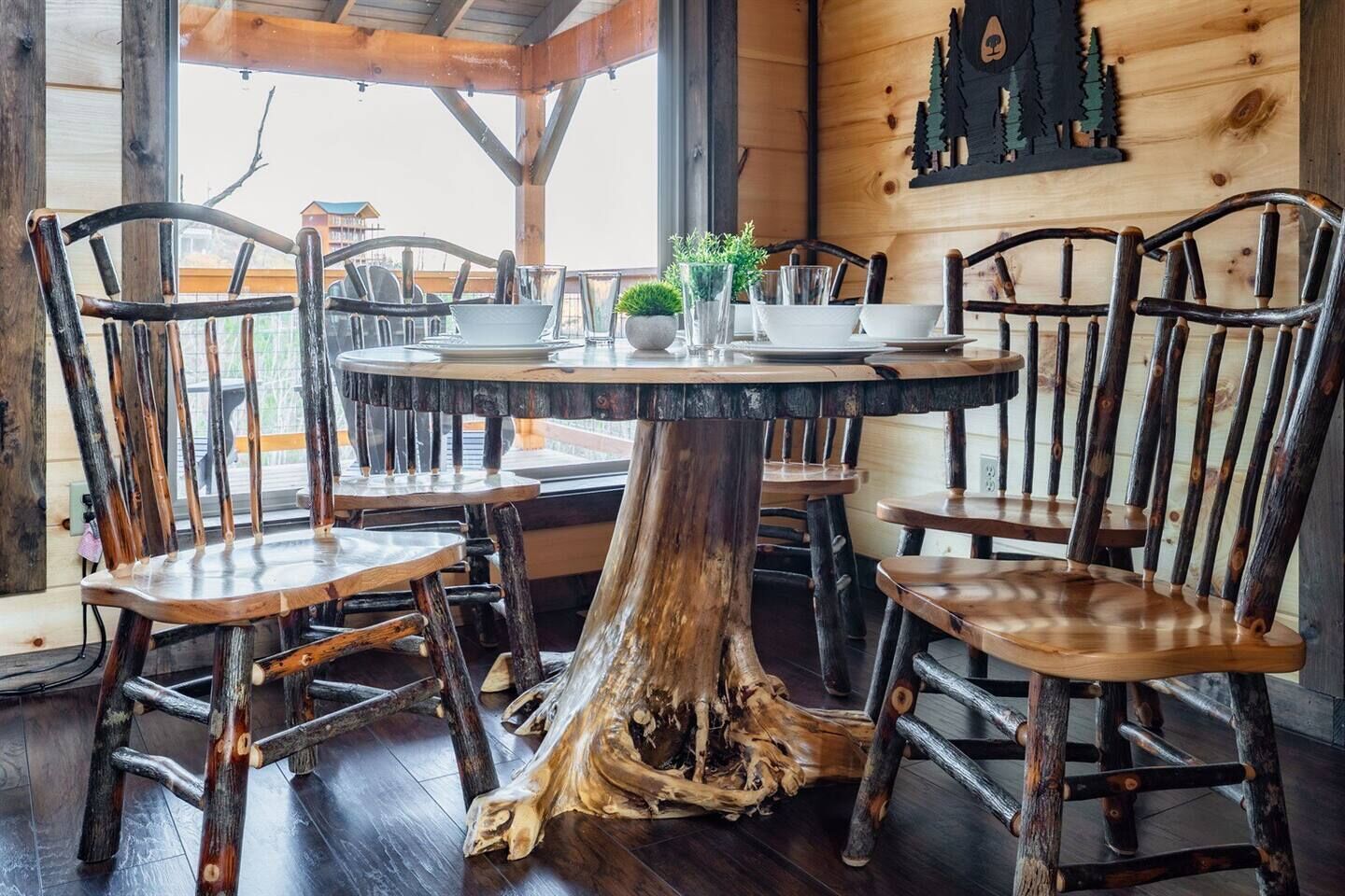 Una mesa de madera rústica con sillas, rodeada por un muro de madera decorado con la silueta de un árbol.