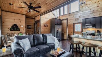 L’intérieur chaleureux d’un chalet avec un canapé en cuir, une table à manger en bois et un coin cuisine équipé d’appareils électroménagers modernes.