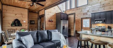 Un interior de cabaña acogedor, con un sofá de cuero, una mesa de comedor de madera y una cocina equipada con electrodomésticos modernos.