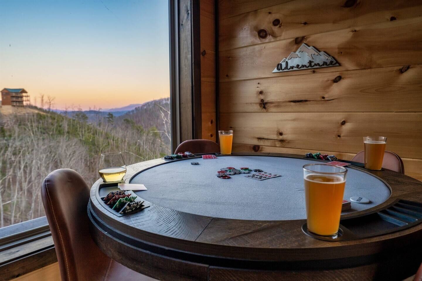 Uma mesa de madeira com vista para montanhas, um jogo de cartas e copos de cerveja.