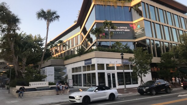 A modern building with a glass facade, a sign for a business office, and a street with cars and pedestrians. - Historic Key West Style Home In South Coconut Grove  Blue House (Coconut Grove)