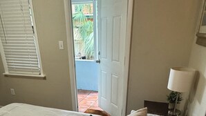A bedroom with a bed, a door leading to an outdoor area, a lamp, and a wall-mounted light fixture. - Historic Key West Style Home In South Coconut Grove  Blue House (Coconut Grove)