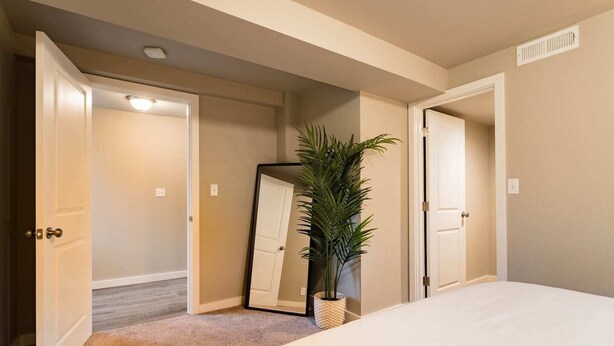 A bedroom with a bed, a potted plant, and two open doors leading to other rooms. - Seattle Launchpad - Cozy and Modern 2 BR Guest Suite (Seattle)