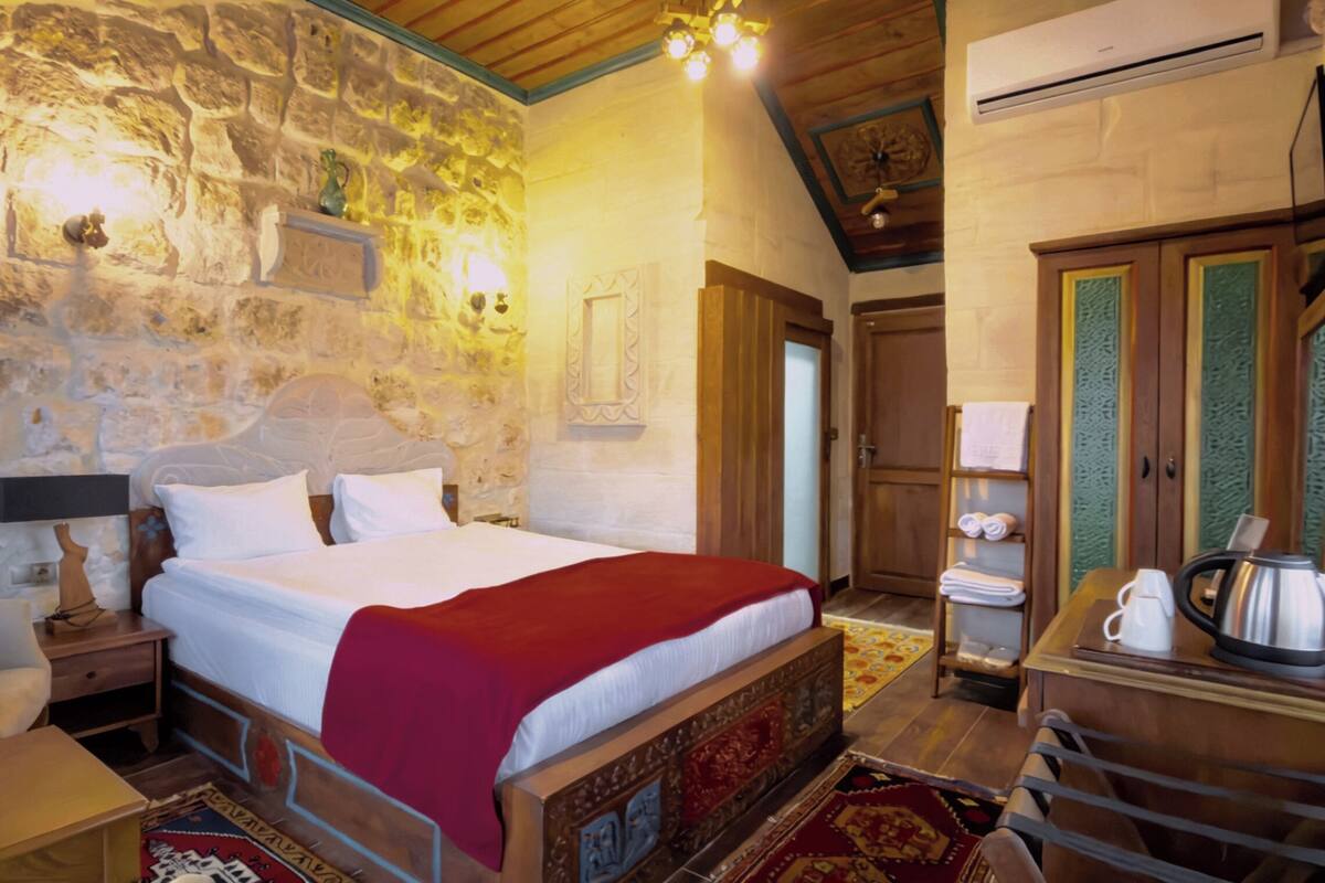 Ein Schlafzimmer mit Steinwand, einem hölzernen Bett, einem Nachttisch, einem Stuhl, einem Tisch mit Wasserkocher und einem Kleiderschrank.