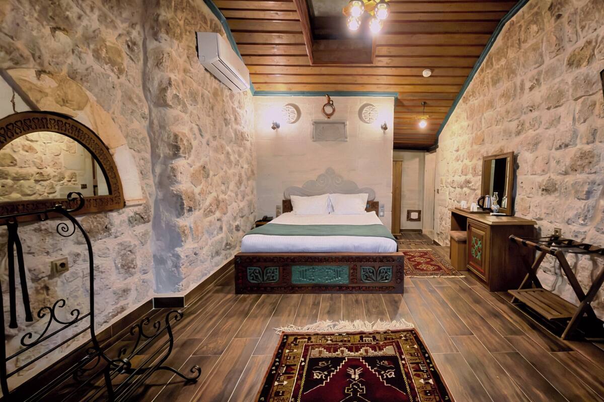 Ein Schlafzimmer mit Steinsturz, Holzboden, Bett, Kommode, Spiegel und Fernseher.