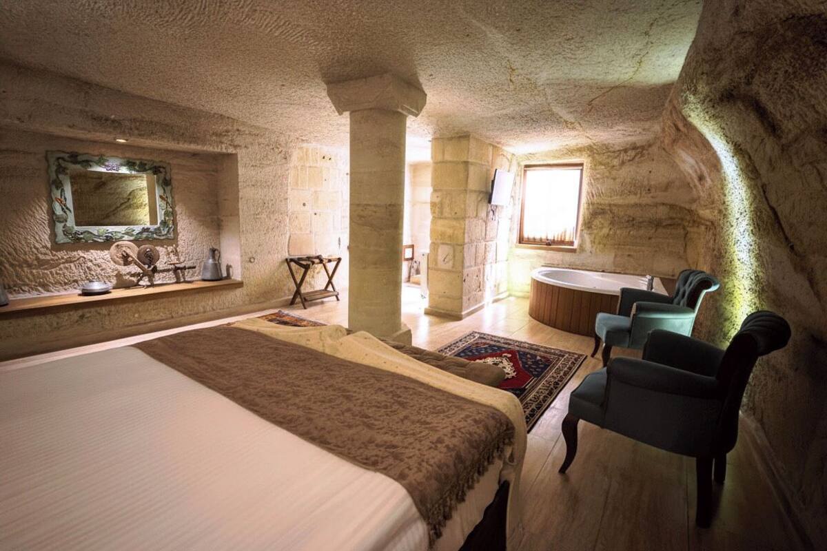 Ein Schlafzimmer mit einem großen Bett, einer Sitzecke mit Sesseln, einer Badewanne und einer Steinwand.
