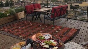 Eine Dachterrasse mit Esstisch, gedeckt für eine Mahlzeit, umgeben von roten Stühlen und Blick auf eine Stadtlandschaft mit Heißluftballons am Himmel.