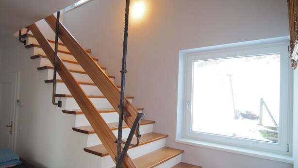 Un escalier en bois avec une rampe, menant à un palier doté d’une fenêtre.