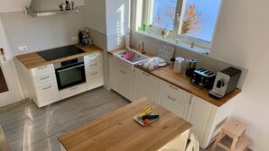 Une cuisine moderne avec des armoires blanches, un plan de travail en bois, un four encastré, un évier et une fenêtre donnant sur les arbres.