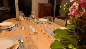 Une table à manger dressée avec de nombreux verres à vin, des assiettes et des couverts, donnant sur un balcon et avec une plante au premier plan.