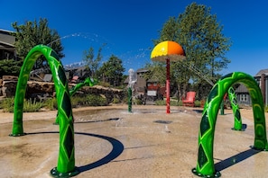 Un espace de jeux aquatiques agrémenté d’arches vertes et d’une fontaine centrale.