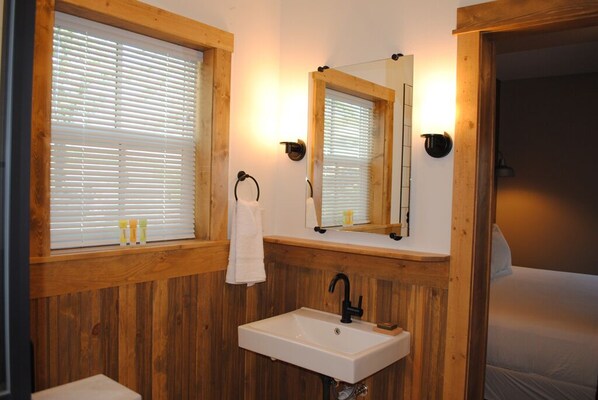 A bathroom with wooden paneling, a white sink, a mirror, and a window with blinds.