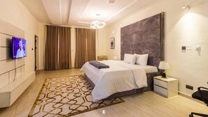 Een moderne hotelkamer met een groot bed, een flatscreen televisie aan de muur, een nachtkastje met een lamp en een kamerkleed met een patroon.