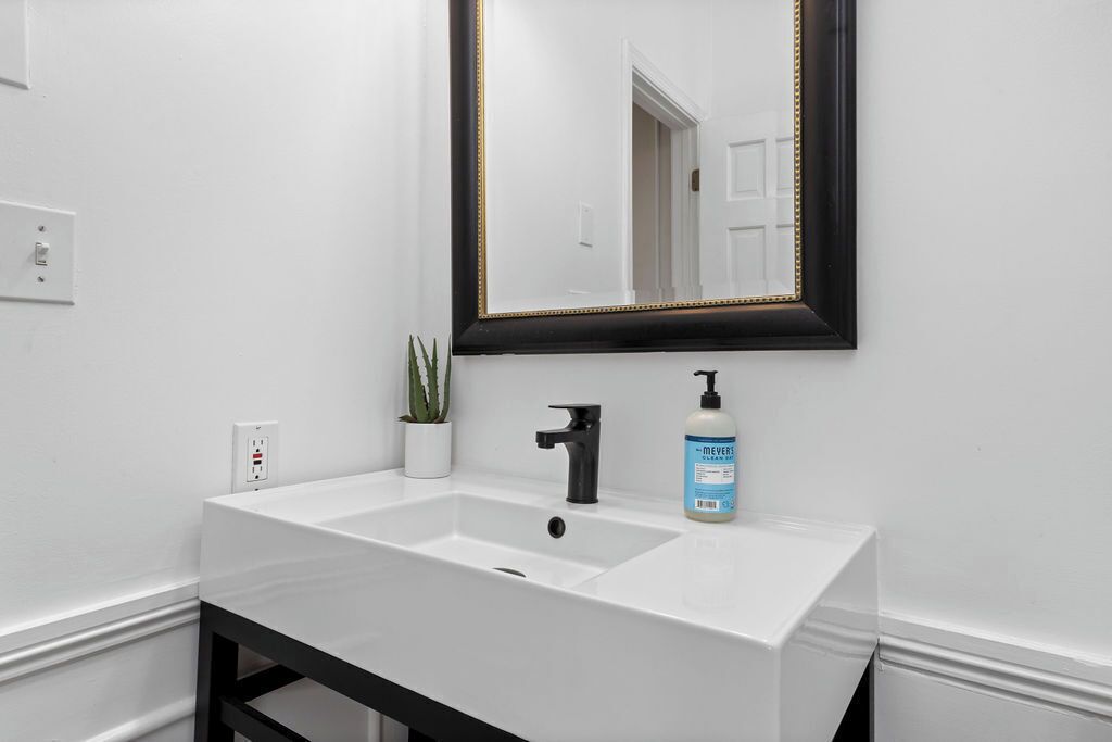 A bathroom with a white sink, black faucet, and a mirror with a black frame.
