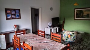 A dining area with a marble table, wooden chairs, a television, a clock, and a colorful chair.