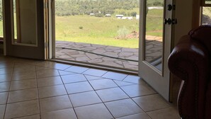 An open door leading to a patio with a view of a green landscape and mountains.