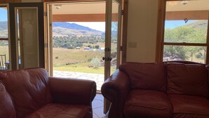 A room with two leather sofas facing a large sliding glass door that opens to a scenic view of a hilly landscape.