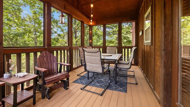 A wooden deck with a table and chairs, a hanging lantern, and a view of trees. - Fourmile Creek Cabin 4 Master Jacuzzi Suites (Branson West)