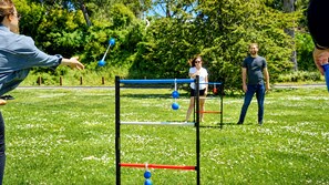 An outdoor activity area with a balance beam and balls, surrounded by grass and trees.