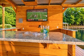 Une terrasse en bois avec un comptoir en granit, un téléviseur fixé au mur et un vase en verre contenant un objet décoratif.