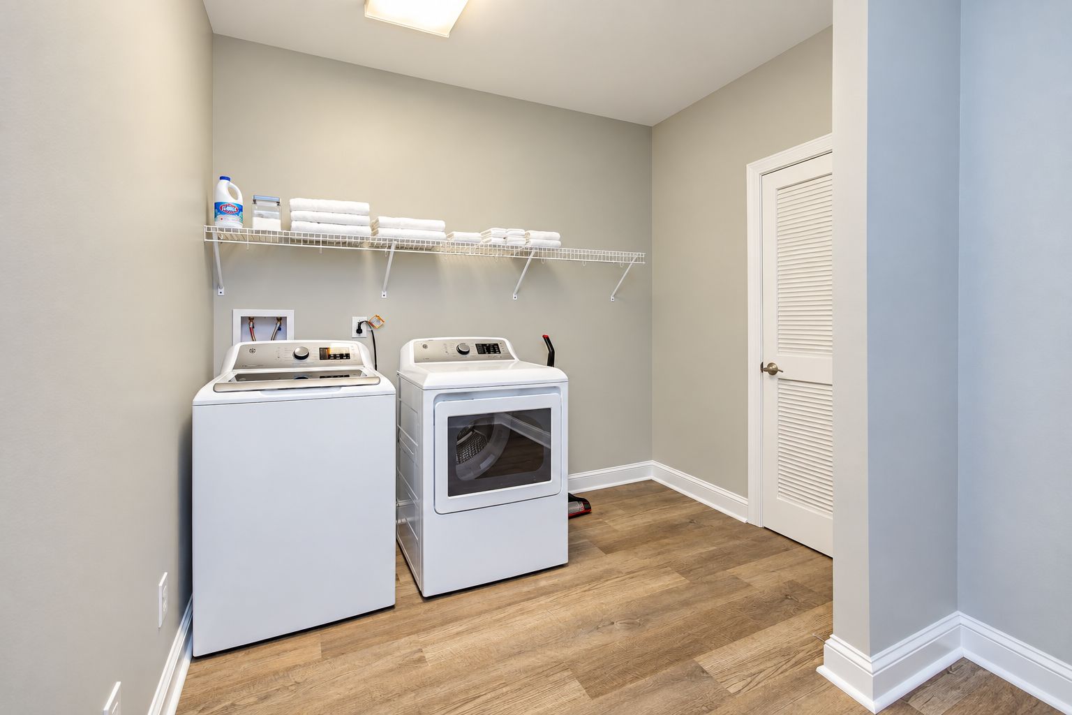 A laundry room with two white washing machines, a dryer, and a shelf with folded towels.