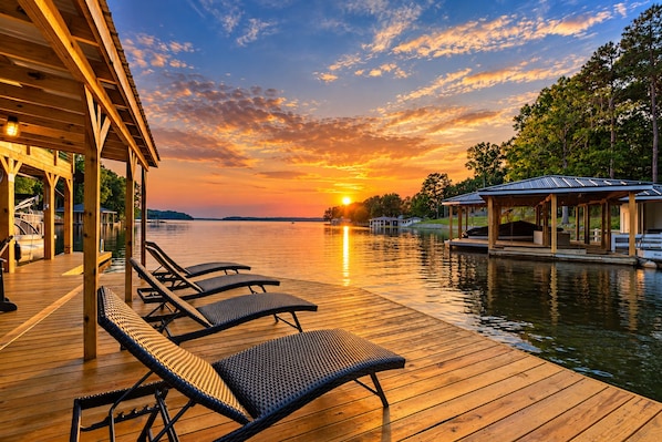 A wooden deck with lounge chairs overlooking a body of water at sunset.