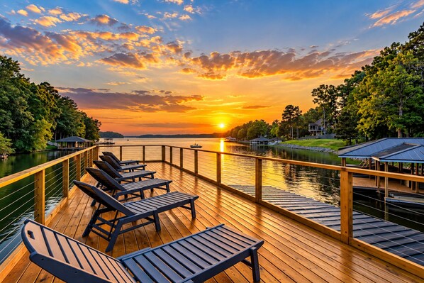 Une terrasse en bois avec des chaises longues donnant sur une étendue d’eau au coucher du soleil.