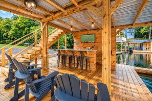 Eine Holzterrasse mit Barbereich, Sitzgelegenheiten im Freien und Blick auf einen See.