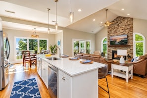 A spacious kitchen with a large island, a dining area with chairs, a living room with a sofa, and a fireplace.