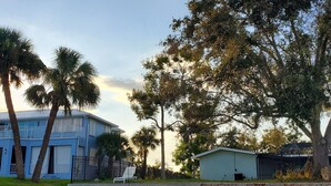 A beachfront property with a blue house, palm trees, and a kayak on the sand. - Peace River Beach House (Port Charlotte)