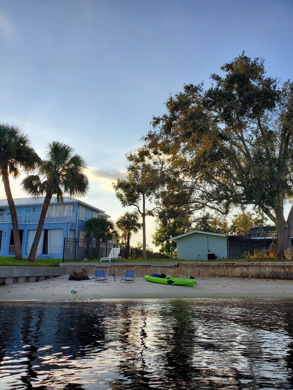 A beachfront property with a blue house, palm trees, and a kayak on the sand. - Peace River Beach House (Port Charlotte)