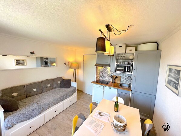 Un espacio habitable compacto con sofá, mesa de comedor y kitchenette.