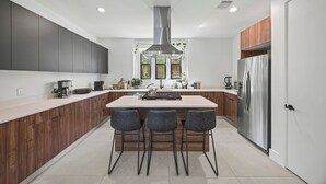 Eine moderne Küche mit Kochinsel, Barhocker, einem Edelstahl-Kühlschrank und Holzschränken.
