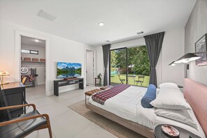 A modern bedroom with a large bed, a desk, and a view of the outdoors. - CASA GRANADA - 5 Bed 4 Bath + FirePit + Patio + Large Backyard + TV's (Conroe)