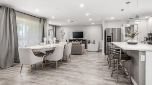 Una cocina moderna con una isla central, taburetes de bar y un comedor con mesa y sillas.