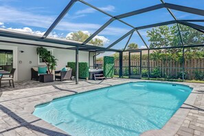 Una piscina con un porche cubierto, mobiliario exterior y vistas al jardín.
