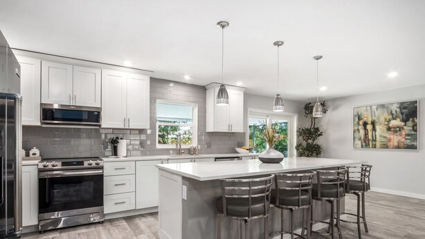Una cocina moderna con armarios blancos, electrodomésticos de acero inoxidable y una isla central con taburetes de bar.