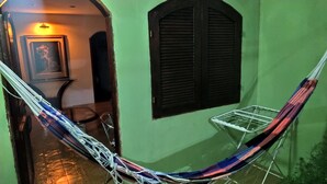 Een kamer met een hangmat, een raam met luiken, een deur naar een andere kamer en een klein rek om kleding te drogen.