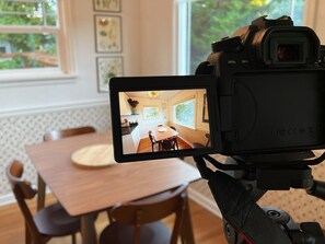 Camera met scherm waarop een kamer te zien is met een eettafel, stoelen en een raam.