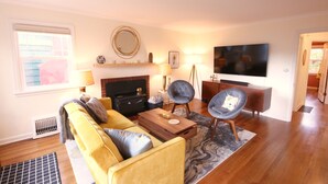 Una sala de estar con sofá, dos sillones, una mesa de centro, chimenea, televisor y ventana.