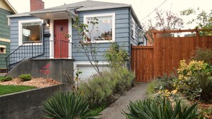 Una casa de dos pisos con una puerta roja, un pequeño porche frontal y una cerca de madera.
