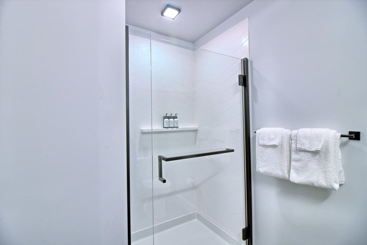 Un baño moderno con cabina de ducha de vidrio, un perchero con dos toallas y un estante con artículos de aseo.